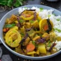 Thai Yellow Chicken Curry in a white bowl with rice placed on a grey table with few ingredients alongside