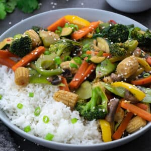 Vegetable stir fry on a grey table along with rice.