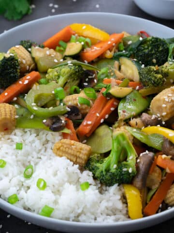 Vegetable stir fry on a grey table along with rice.