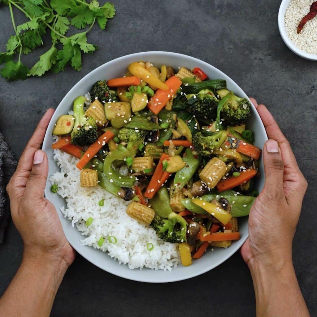 Serving the healthy and easy Vegetable stir Fry over rice in a white bowl.