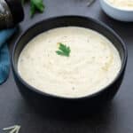 Alfredo Sauce in a black bowl with few ingredients around.