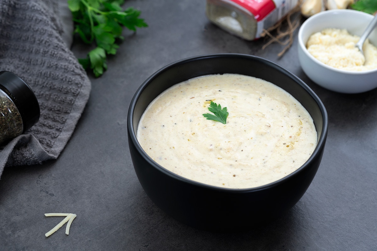 Alfredo Sauce in a black bowl with few ingredients around.