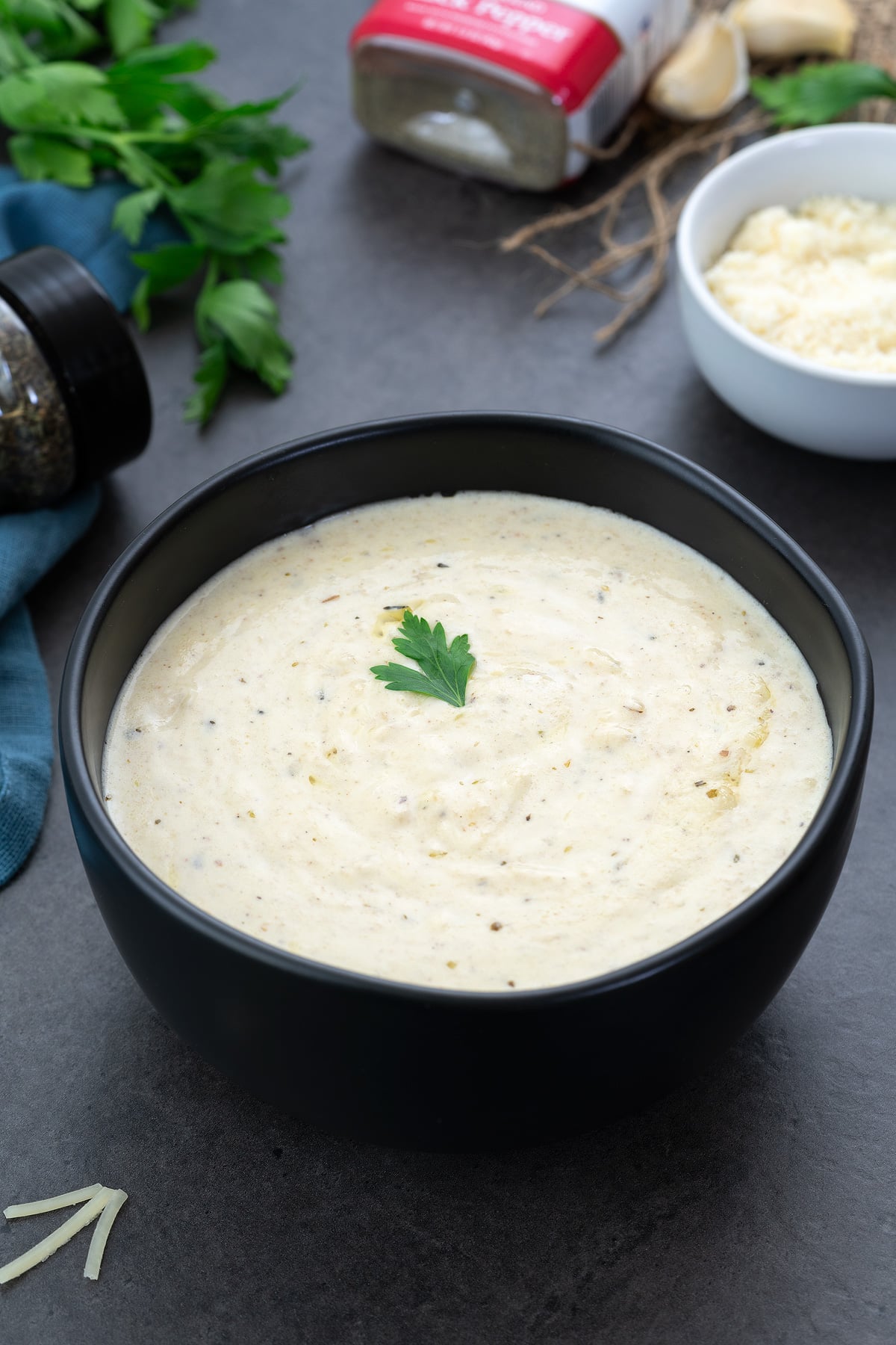 Alfredo Sauce in a black bowl with few ingredients around.