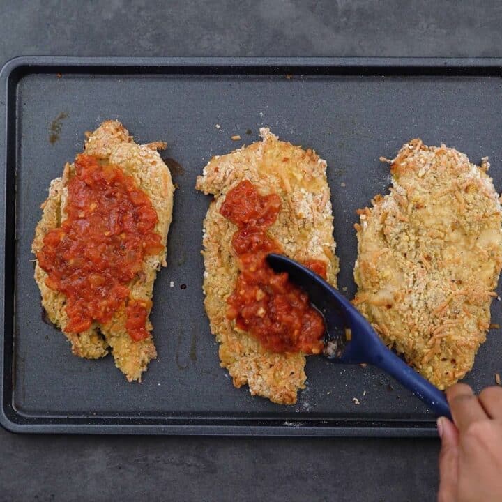Topping the baked breaded chicken breast with marinara sauce.