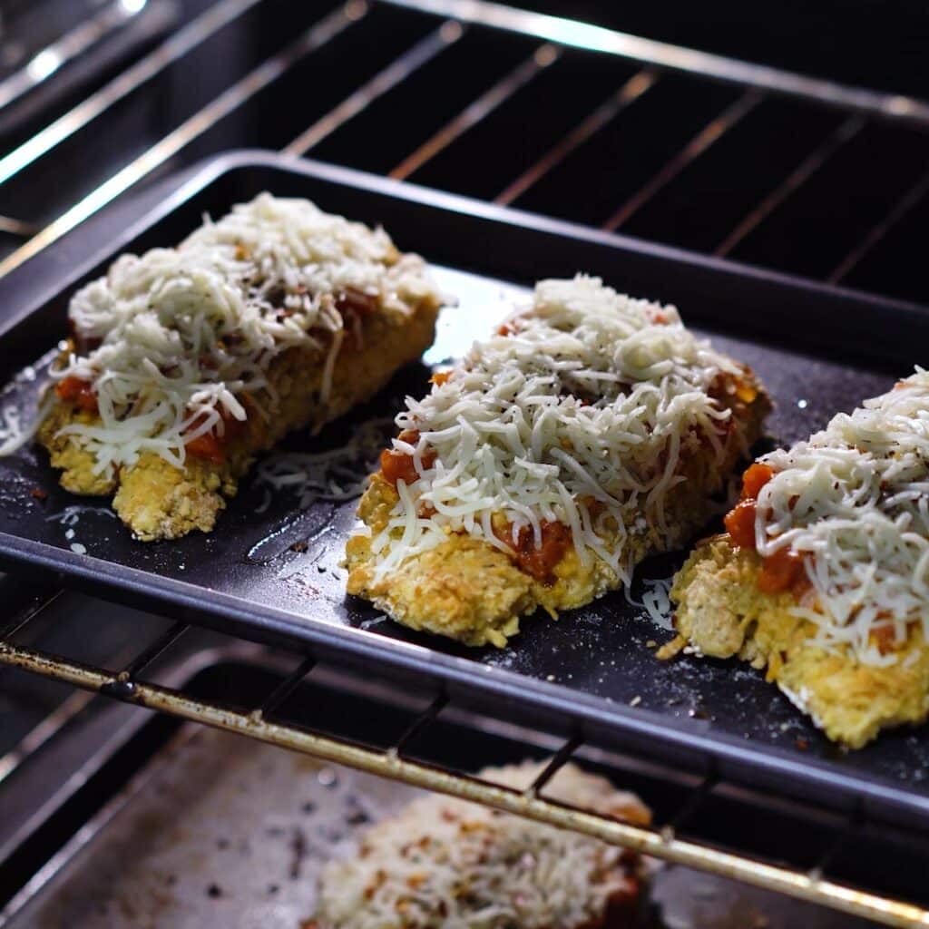 Chicken breast topped with sauce and cheese placed inside the oven.