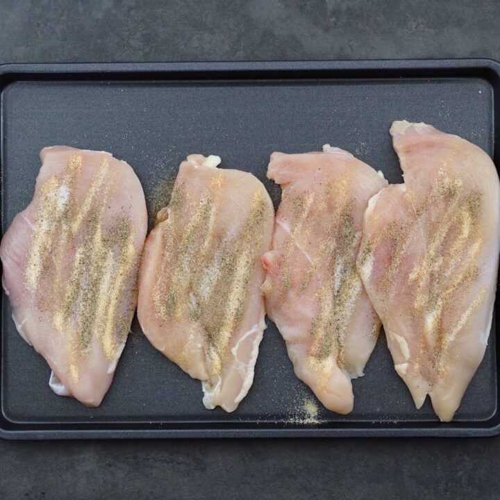 Chicken breast with seasoning on the baking tray.
