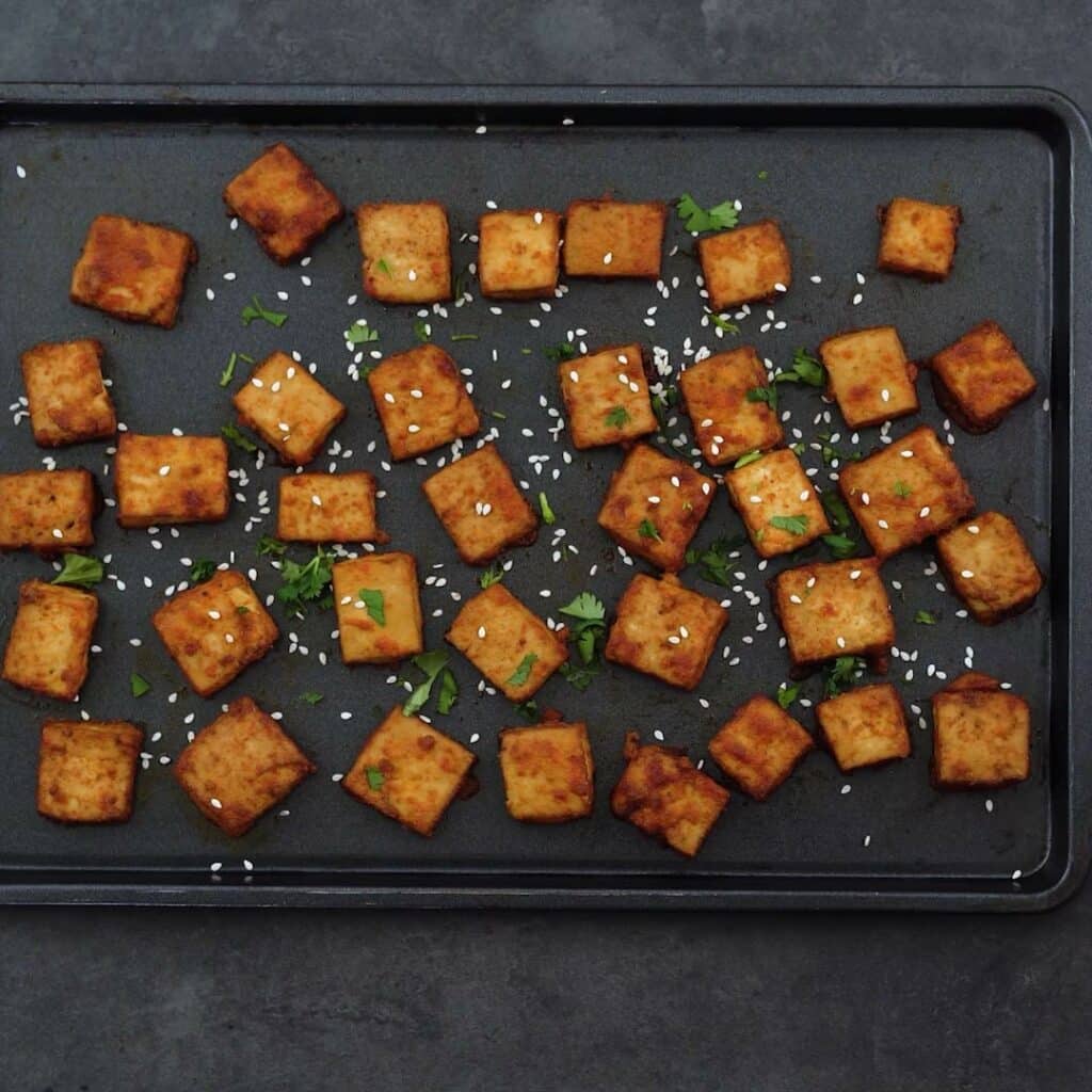 Crispy baked tofu garnished with sesame seeds and cilantro leaves.