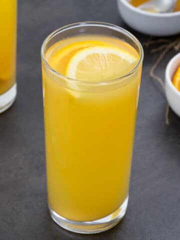 Homemade electrolyte drink in two glasses with orange slices and honey around.