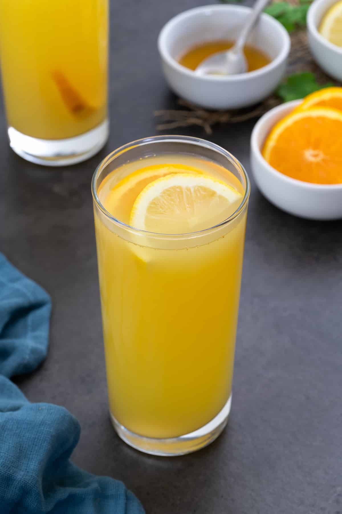 Homemade electrolyte drink in two glasses with orange slices and honey around.