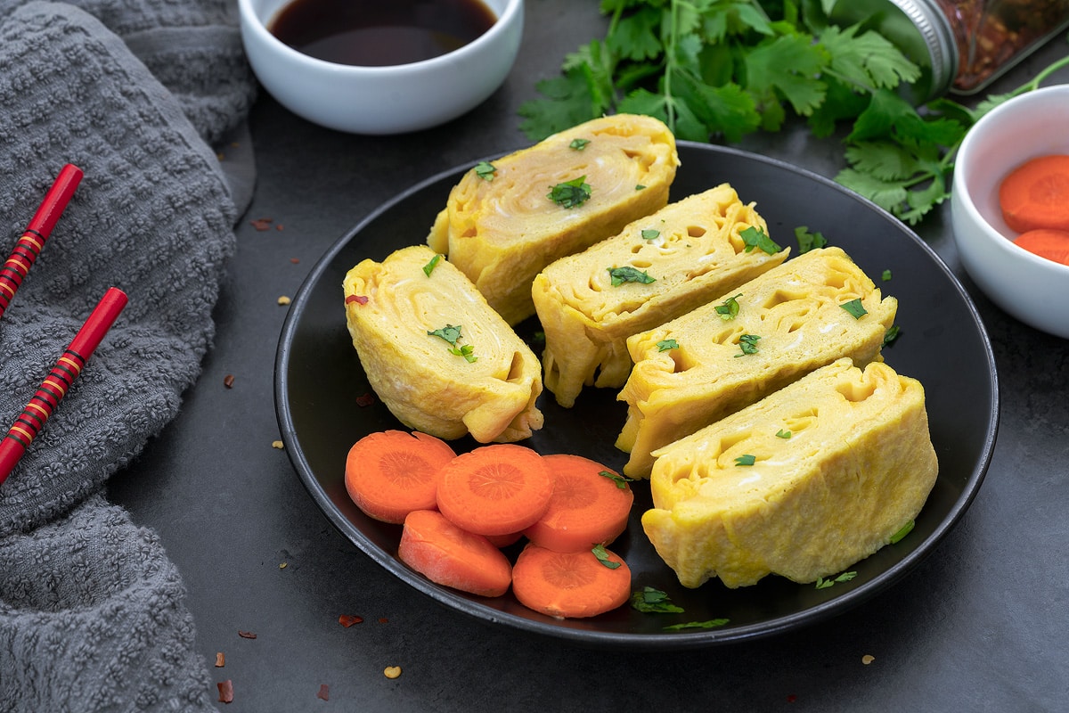Tamagoyaki (Japanese rolled omelette) placed on a black plate with cut carrot pieces.