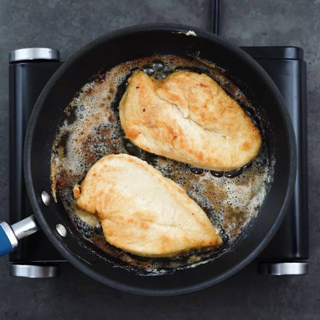 Chicken breast frying in a pan.