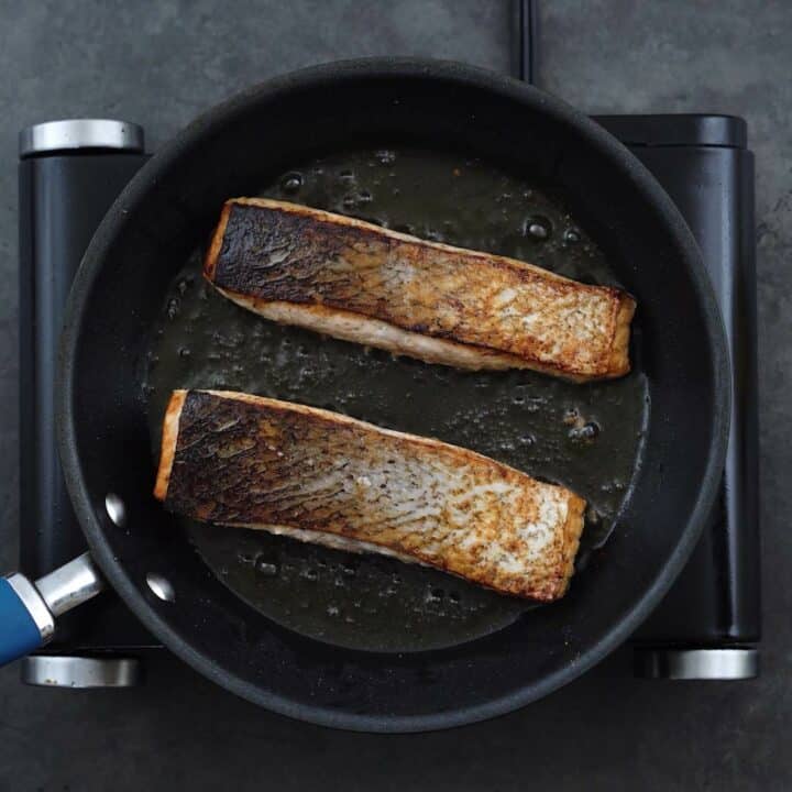 Salmon fillets frying facing skin side up in a pan.
