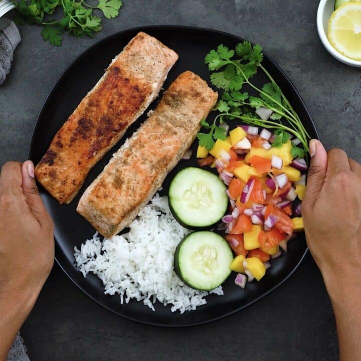 Serving Pan Fried Salmon with rice and salad on a black plate.