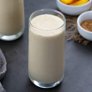 Peach smoothie in a glass with whole and cut peach with sugar around.