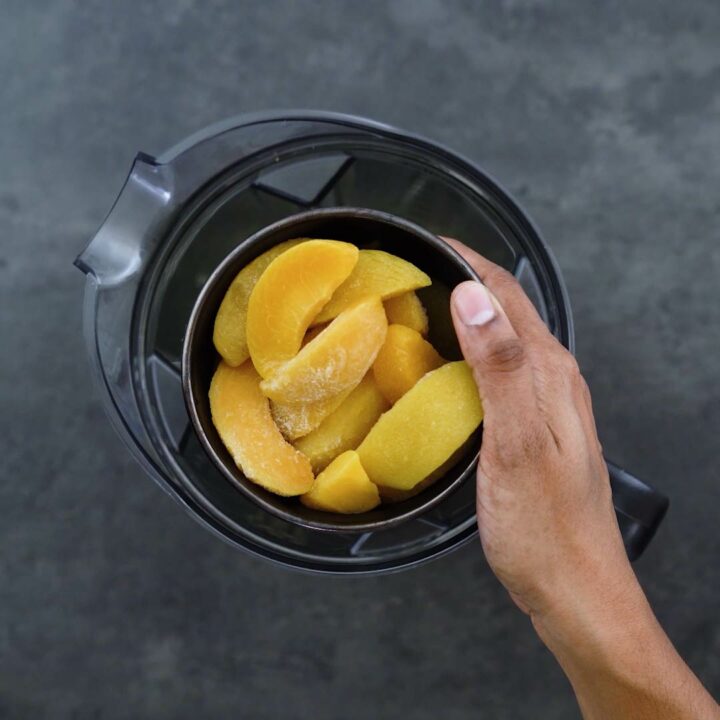 Adding frozen peaches into the blender jar.