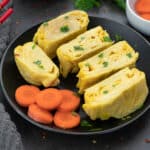 Tamagoyaki (Japanese rolled omelette) placed on a black plate with cut carrot pieces.