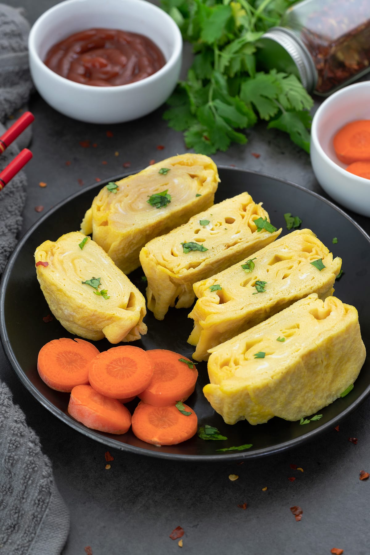 Tamagoyaki (Japanese rolled omelette) placed on a black plate with cut carrot pieces.