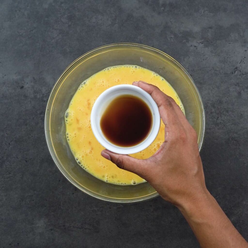 Adding soy sauce into the beaten eggs.