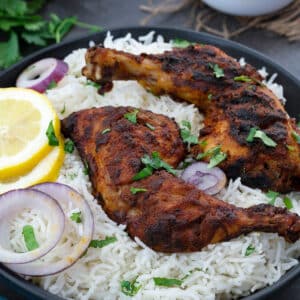 Tandoori Chicken in a black bowl with rice, lemon and onion slices.