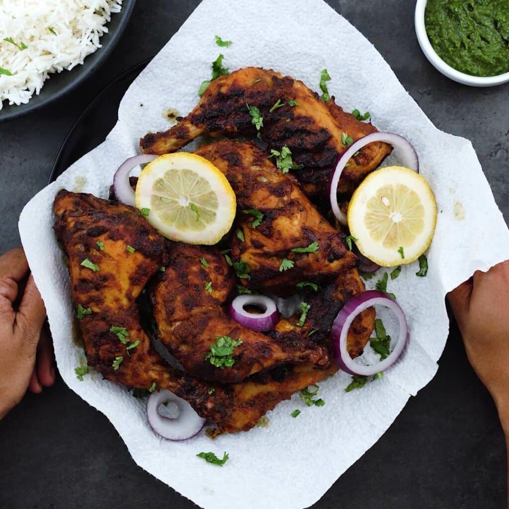 Serving Tandoori Chicken with lemon wedges, lemon slices and green chutney alongside.
