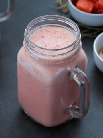 Watermelon Smoothie in a mug with watermelon pieces and a strawberry around it.