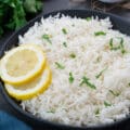 Cooked Basmati Rice in a black bowl with lemon slices and greens, blue towel around.