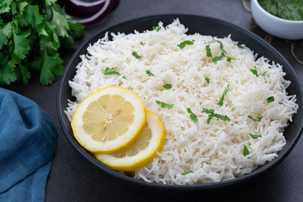 Cooked Basmati Rice in a black bowl with lemon slices and greens, blue towel around.