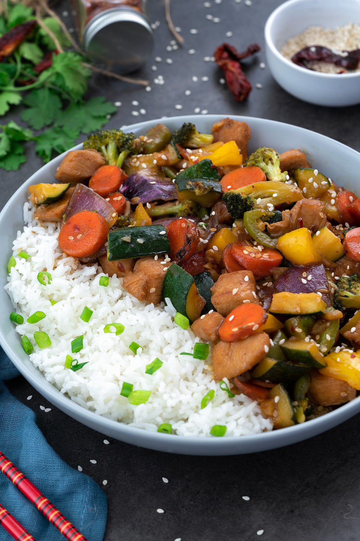 Chicken Stir Fry in a white bowl with rice with few ingredients around.