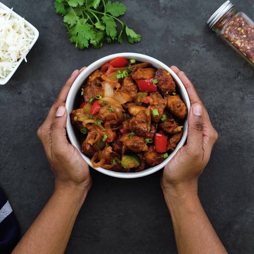 Serving Chilli Chicken in a white bowl with rice alongside.