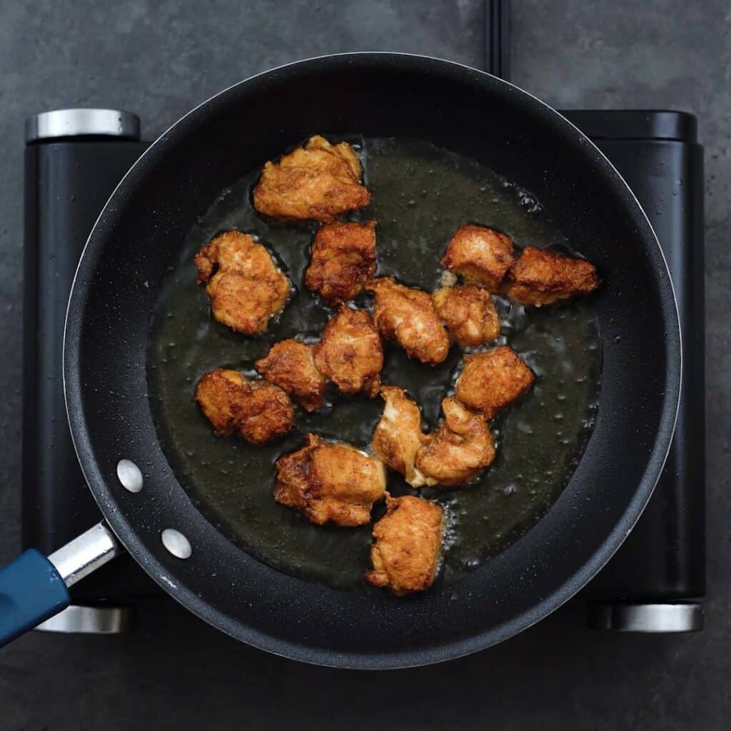 Chicken frying in a pan with oil.