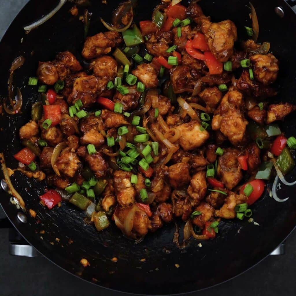 Chilli Chicken garnished with spring onions in a wok.