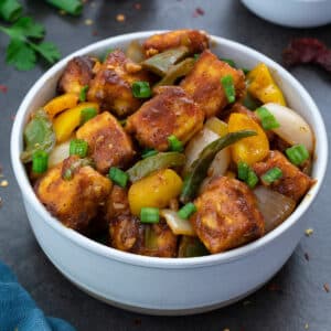 Chilli Paneer in a white bowl with few ingredients around.
