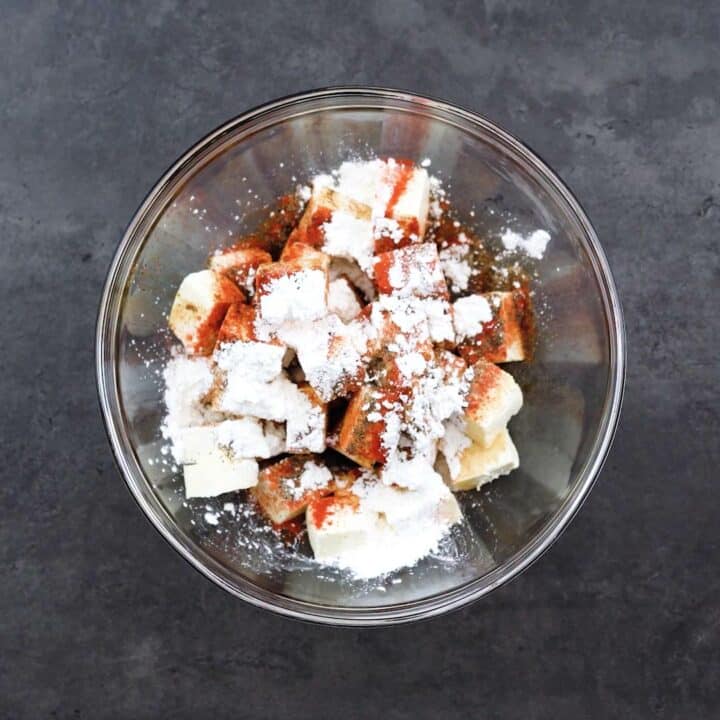 Paneer with marinating ingredients in a glass bowl.