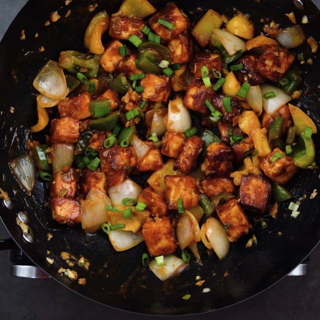 Chilli Paneer garnished with spring onions in a wok.