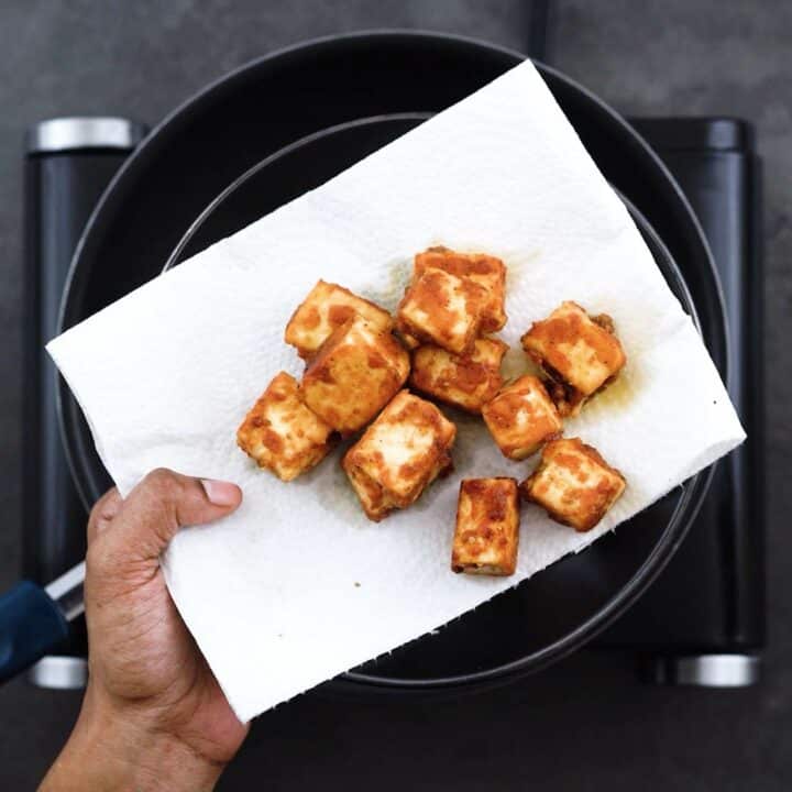 Golden fried Paneer in a black plate with tissue paper.