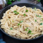 Fettuccine Alfredo in a black bowl placed on a grey table.