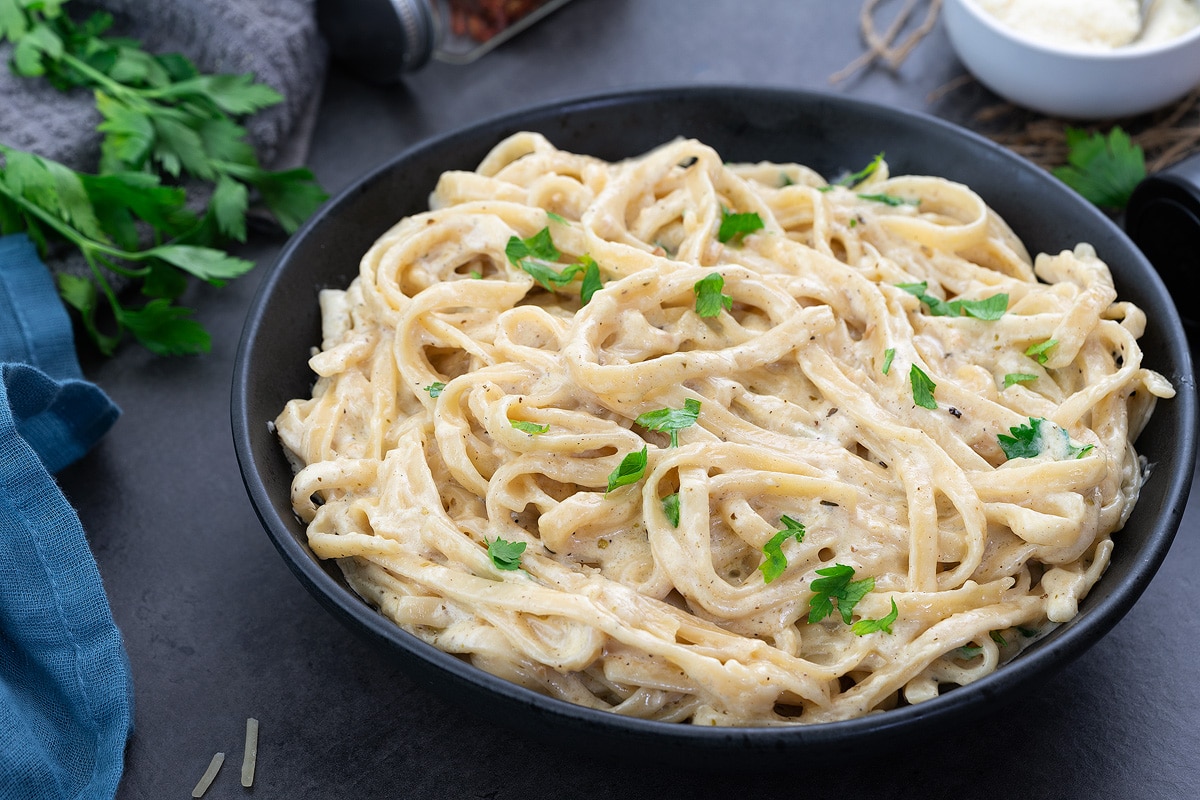 Fettuccine Alfredo in a black bowl placed on a grey table.