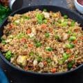 Homemade Fried Rice in a black bowl on a grey table with few ingredients around.
