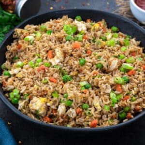 Homemade Fried Rice in a black bowl on a grey table with few ingredients around.