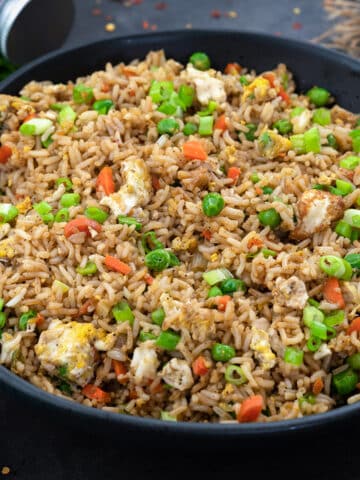 Homemade Fried Rice in a black bowl on a grey table with few ingredients around.