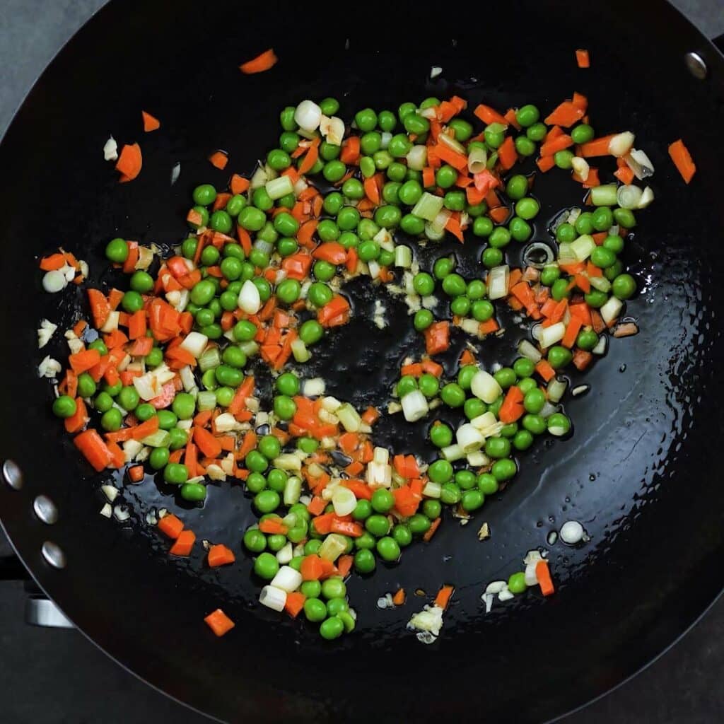 Stir fried carrots, peas along with garlic and green onions in a wok.