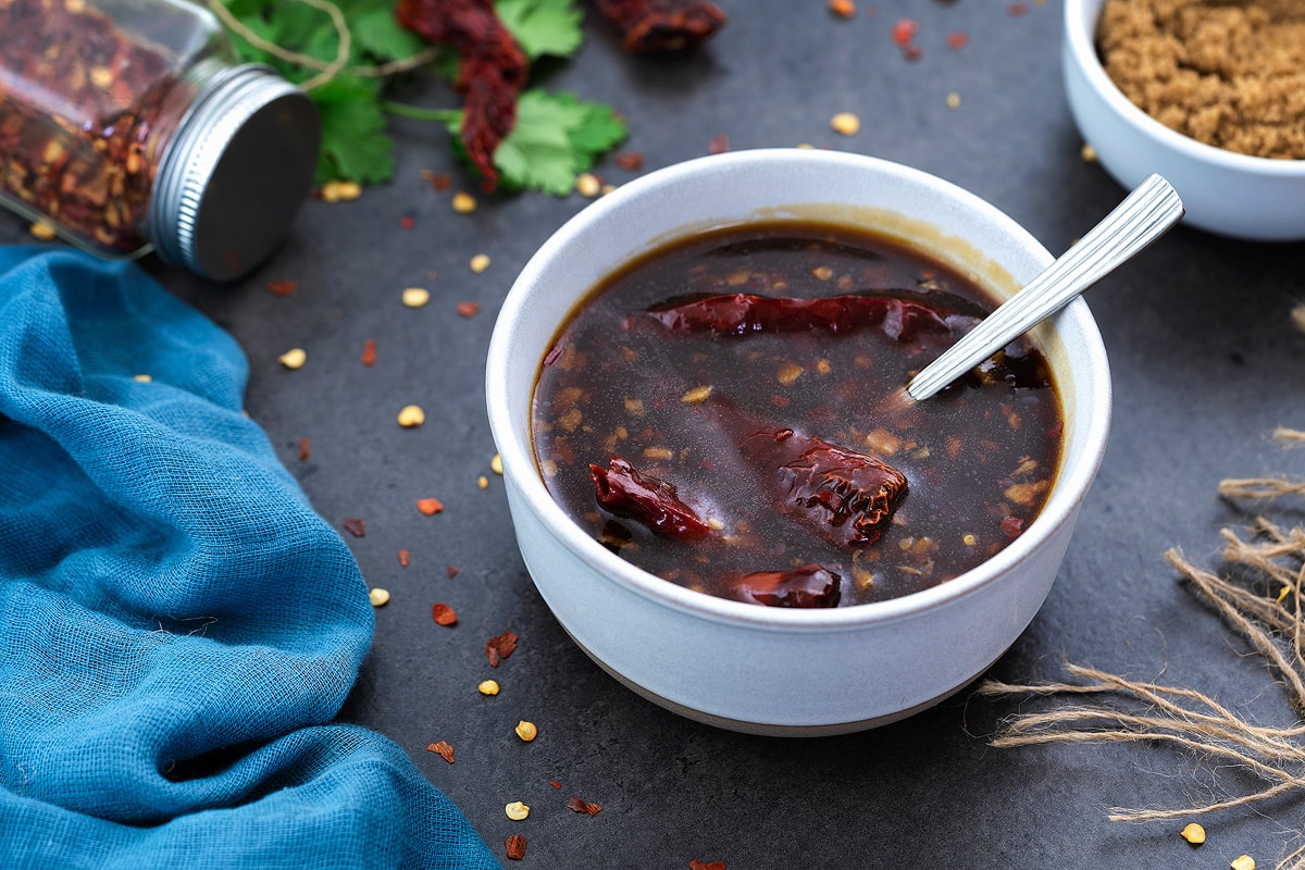 Stir fry sauce in a white bowl on a grey table with few ingredients around.