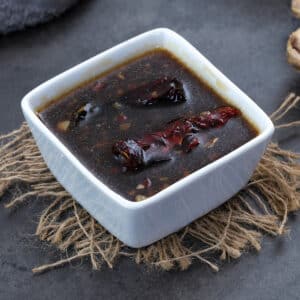 Teriyaki Sauce in a white square cup on a grey table with few ingredients around.