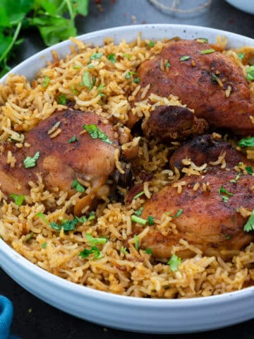 Chicken and Rice in a white bowl on a grey table with few ingredients around.