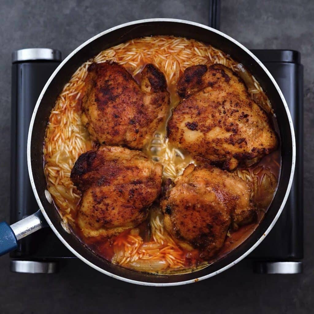 Fried chicken thighs over rice in a pot.