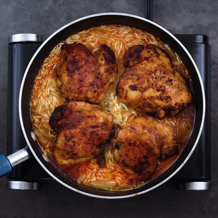 Fried chicken thighs over rice in a pot.