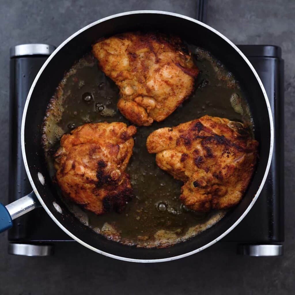 Browned Chicken thighs in a frying pan.