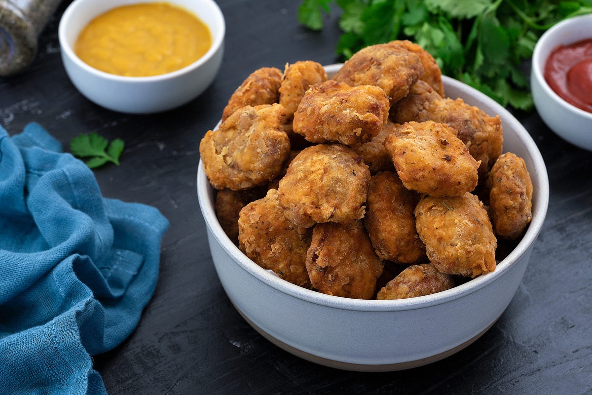 Crispy Homemade chicken nuggets in a white bowl with few ingredients around.