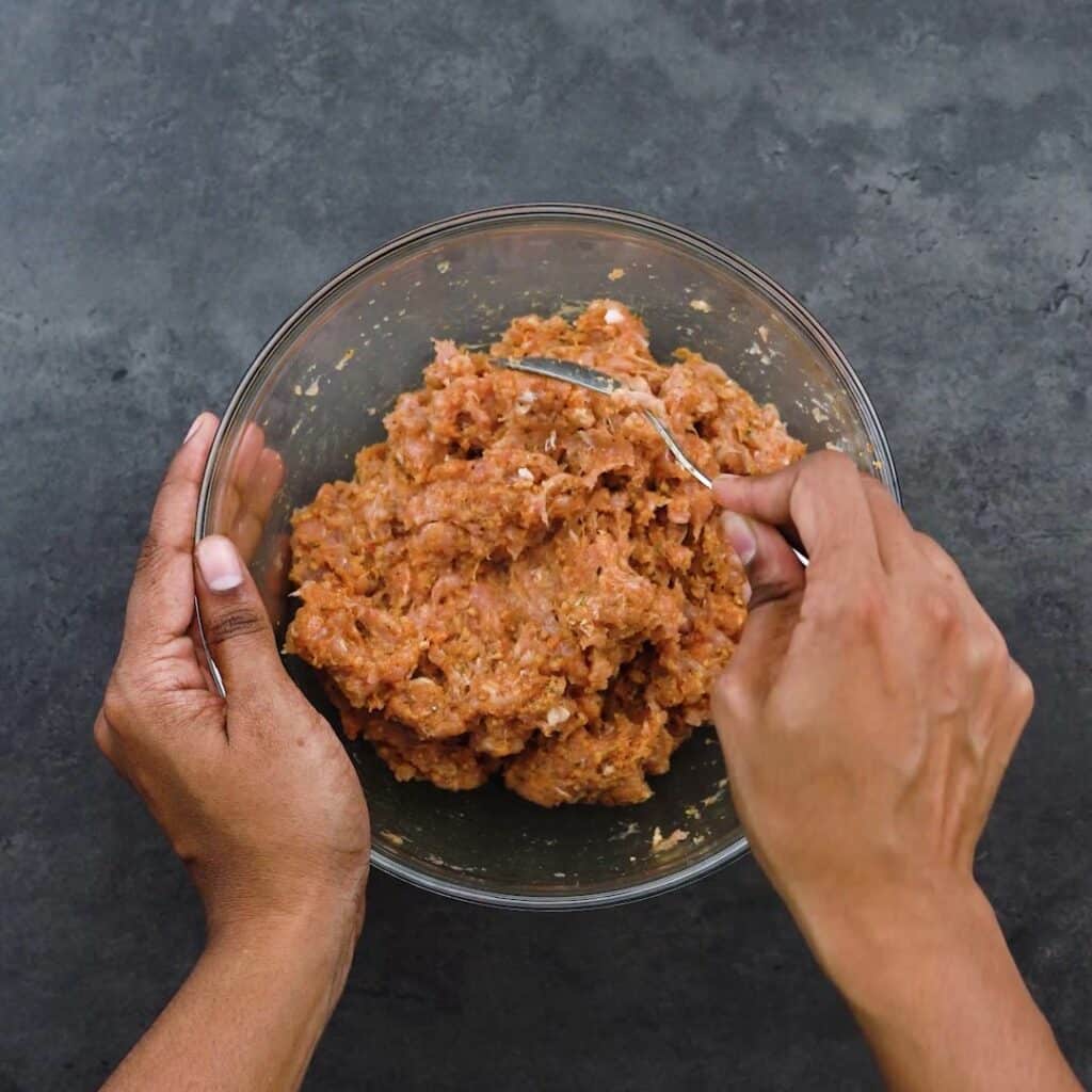 Mixing ground chicken with seasonings.