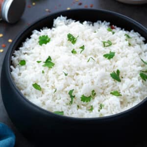 Perfectly cooked fluffy rice in a black bowl on a grey table, with few ingredients around.